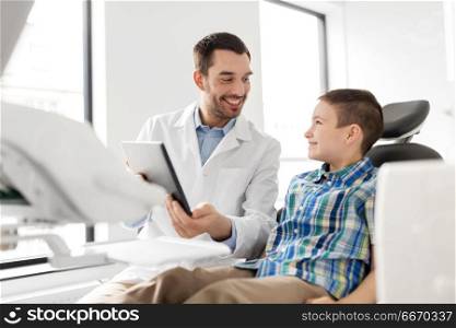 medicine, dentistry and healthcare concept - smiling male dentist showing tablet pc computer to kid patient at dental clinic. dentist showing tablet pc to kid patient at clinic. dentist showing tablet pc to kid patient at clinic