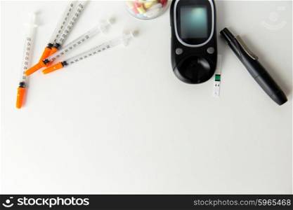 medicine, diabetes, advertisement and health care concept - close up of glucometer with blood sugar test stripe, insulin injection syringes and pills on table