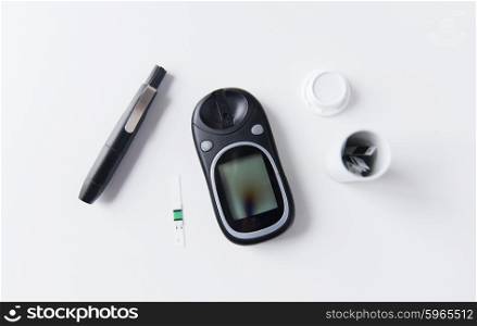medicine, diabetes and health care concept - close up of glucometer with stick and blood sugar test stripes container on table