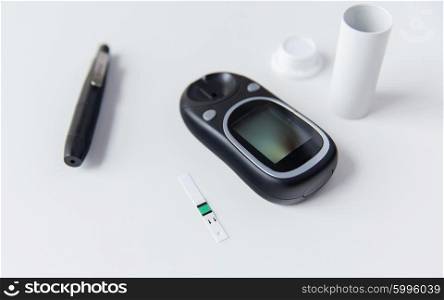 medicine, diabetes and health care concept - close up of glucometer with stick and blood sugar test stripes container on table