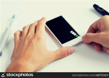 medicine, diabetes, glycemia, health care and people concept - close up of man with smartphone checking blood sugar level by glucometer at home