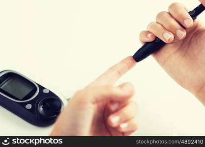 medicine, diabetes, glycemia, health care and people concept - close up of woman checking blood sugar level by glucometer at home