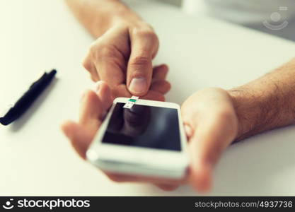 medicine, diabetes, glycemia, health care and people concept - close up of man with smartphone checking blood sugar level by glucometer at home. close up of man with smartphone making blood test