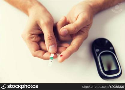 medicine, diabetes, glycemia, health care and people concept - close up of man checking blood sugar level by glucometer at home. close up of man checking blood sugar by glucometer