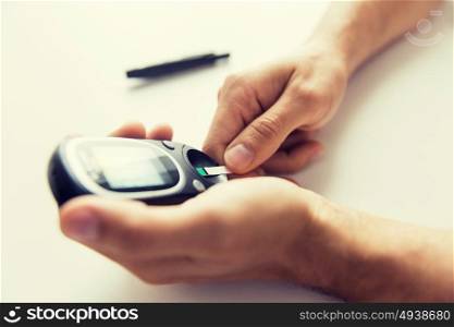 medicine, diabetes, glycemia, health care and people concept - close up of man checking blood sugar level with glucometer and test stripe at home. close up of man checking blood sugar by glucometer