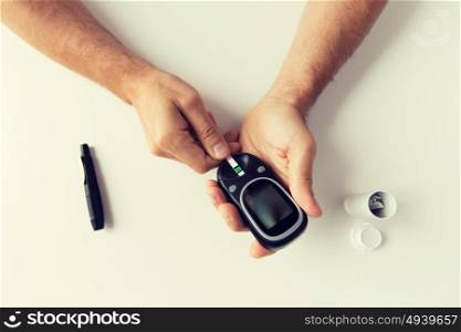 medicine, diabetes, glycemia, health care and people concept - close up of man checking blood sugar level with glucometer and test stripe at home. close up of man checking blood sugar by glucometer