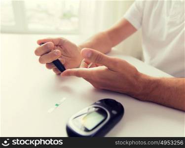 medicine, diabetes, glycemia, health care and people concept - close up of man checking blood sugar level by glucometer at home. close up of man checking blood sugar by glucometer