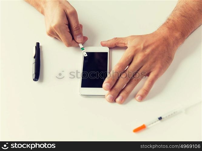 medicine, diabetes, glycemia, health care and people concept - close up of man with smartphone checking blood sugar level by glucometer at home. close up of man with smartphone making blood test
