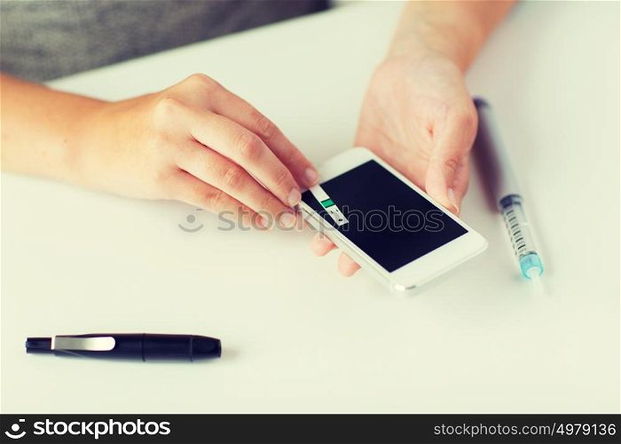 medicine, diabetes, glycemia, health care and people concept - close up of woman hands with smartphone checking blood sugar level by glucometer at home. close up of woman with smartphone doing blood test