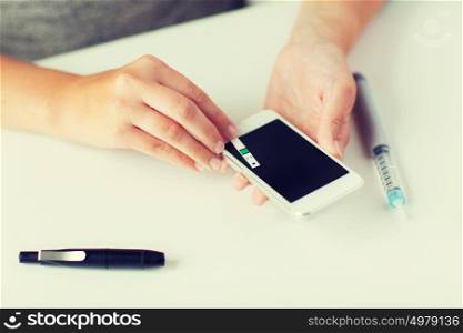 medicine, diabetes, glycemia, health care and people concept - close up of woman hands with smartphone checking blood sugar level by glucometer at home. close up of woman with smartphone doing blood test