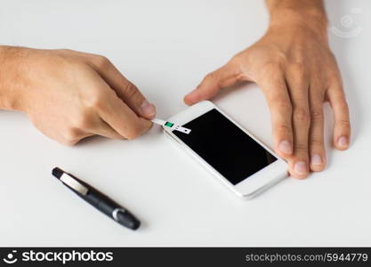 medicine, diabetes, glycemia, health care and people concept - close up of man with smartphone checking blood sugar level by glucometer at home