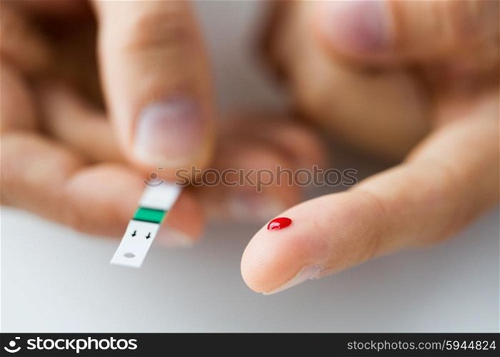 medicine, diabetes, glycemia, health care and people concept - close up of male finger with blood drop and test stripe