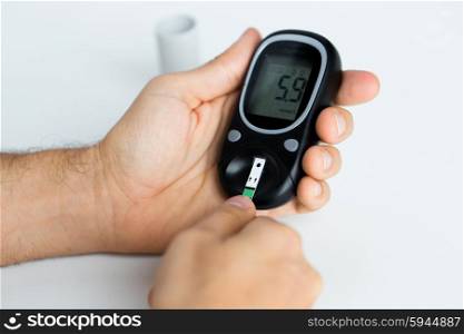 medicine, diabetes, glycemia, health care and people concept - close up of man checking blood sugar level by glucometer and test stripe at home