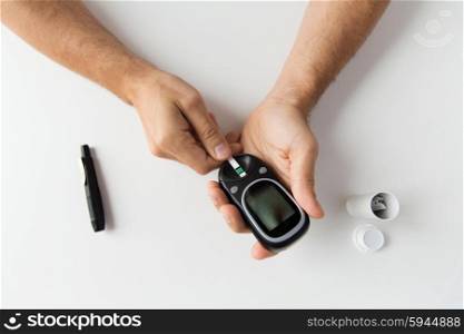 medicine, diabetes, glycemia, health care and people concept - close up of man checking blood sugar level with glucometer and test stripe at home