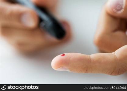 medicine, diabetes, glycemia, health care and people concept - close up of male finger with blood drop and glucometer