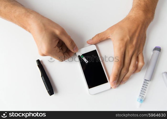 medicine, diabetes, glycemia, health care and people concept - close up of man with smartphone checking blood sugar level by glucometer at home