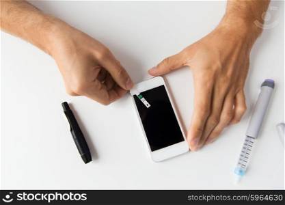 medicine, diabetes, glycemia, health care and people concept - close up of man with smartphone checking blood sugar level by glucometer at home
