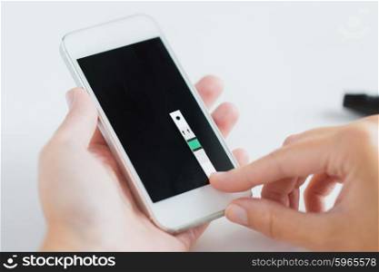 medicine, diabetes, glycemia, health care and people concept - close up of woman hands with smartphone and test stripe checking blood sugar level by glucometer application at home