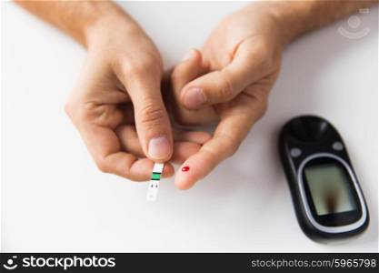 medicine, diabetes, glycemia, health care and people concept - close up of man checking blood sugar level by glucometer at home