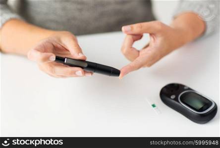 medicine, diabetes, glycemia, health care and people concept - close up of woman checking blood sugar level by glucometer at home