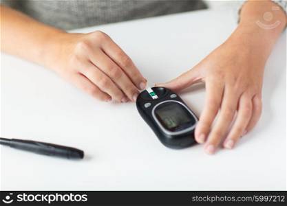 medicine, diabetes, glycemia, health care and people concept - close up of woman hands with glucometer and test stripe checking blood sugar level at home