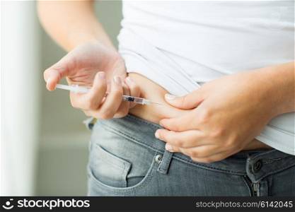 medicine, diabetes, glycemia, health care and people concept - close up of woman with syringe making insulin injection to himself at home