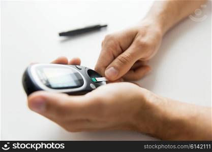 medicine, diabetes, glycemia, health care and people concept - close up of man checking blood sugar level with glucometer and test stripe at home