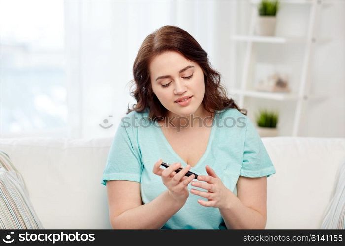 medicine, diabetes, glycemia, health care and people concept - young plus size woman checking blood sugar level by glucometer at home