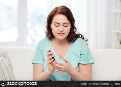 medicine, diabetes, glycemia, health care and people concept - young plus size woman checking blood sugar level by glucometer at home