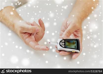medicine, diabetes, healthcare and old people concept - senior man with glucometer checking blood sugar level at home over snow. senior man with glucometer checking blood sugar