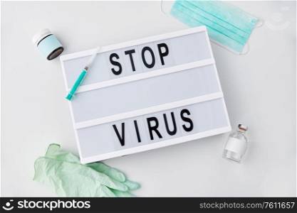 medicine, epidemic and healthcare concept - lightbox with stop virus caution words, protective mask, gloves and syringe with drug on white background. lightbox with stop virus caution words
