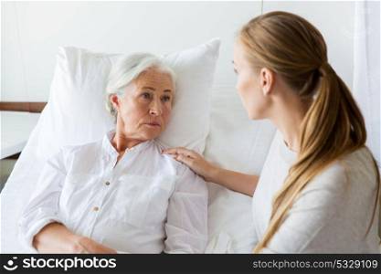medicine, family, healthcare and people concept - daughter visiting and cheering her mother lying in bed at hospital ward. daughter visiting her senior mother at hospital