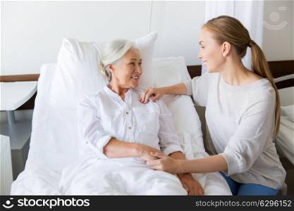 medicine, family, healthcare and people concept - daughter visiting and cheering her mother lying in bed at hospital ward. daughter visiting senior mother at hospital