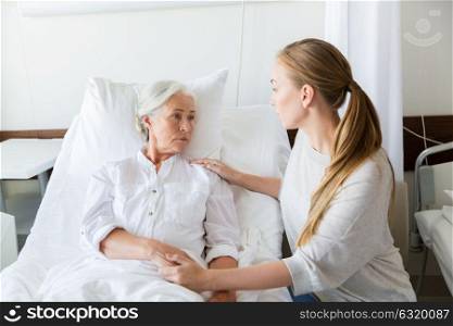 medicine, family, healthcare and people concept - daughter visiting and cheering her mother lying in bed at hospital ward. daughter visiting her senior mother at hospital
