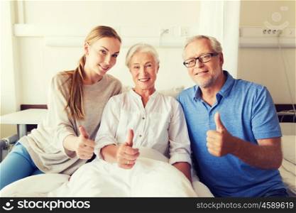 medicine, family support, gesture, health care and people concept - happy senior man and young woman visiting her grandmother and showing thumbs up at hospital ward