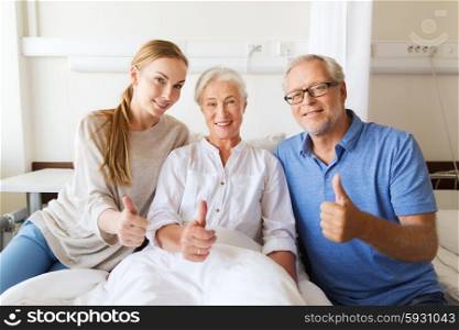 medicine, family support, gesture, health care and people concept - happy senior man and young woman visiting her grandmother and showing thumbs up at hospital ward