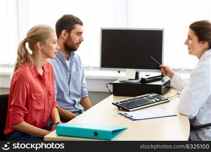 medicine, fertility and healthcare concept - couple and doctor pointing at computer monitor screen at family planning clinic. couple and doctor pointing at computer at clinic