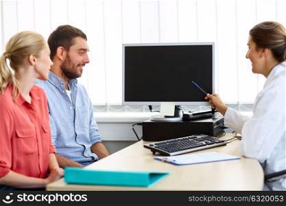 medicine, fertility and healthcare concept - happy couple and doctor pointing at computer monitor screen at family planning clinic. couple and doctor pointing at computer at clinic