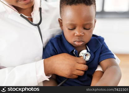 medicine, healtcare, pediatry and people concept - close up of african american female doctor or pediatrician with stethoscope listening to baby patient on medical exam at clinic. doctor with stethoscope and baby patient at clinic