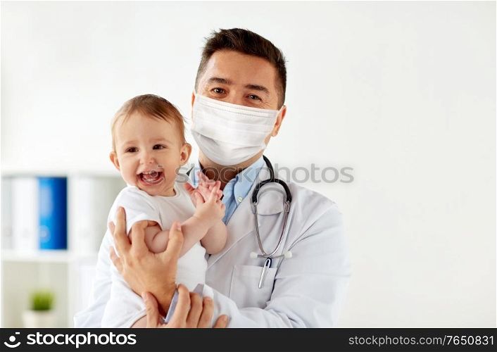 medicine, healtcare, pediatry and people concept - doctor or pediatrician wearing face protective medical mask for protection from virus disease holding baby at hospital. doctor or pediatrician in mask with baby at clinic