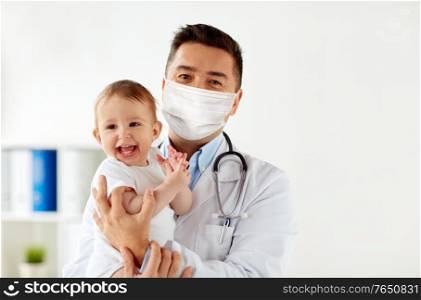 medicine, healtcare, pediatry and people concept - doctor or pediatrician wearing face protective medical mask for protection from virus disease holding baby at hospital. doctor or pediatrician in mask with baby at clinic
