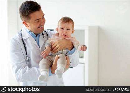 medicine, healtcare, pediatry and people concept - happy doctor or pediatrician holding sad crying baby girl on medical exam at clinic. happy doctor or pediatrician with baby at clinic