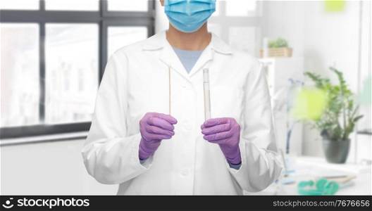 medicine, health and coronavirus concept - close up of female doctor in gloves and mask with test tube and cotton swab over medical office at hospital background. female doctor with test tube and cotton swab