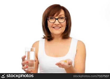 medicine, health and old people concept - smiling senior woman in glasses with glass of water and pills over white background. senior woman with glass of water and pills