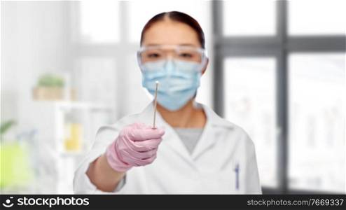 medicine, health and pandemic concept - close up of young asian female doctor or scientist in medical mask and goggles holding test cotton swab over medical office at hospital on background. asian female doctor in mask with test cotton swab
