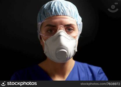 medicine, health and pandemic concept - close up of young female doctor or nurse wearing goggles, hat and face protective mask or respirator for protection from virus disease over black background. doctor in goggles and protective face mask