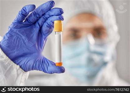 medicine, health and pandemic concept - close up of young female doctor or scientist in face protective medical mask, goggles and gloves holding beaker with virus test. scientist in protective mask with test tube
