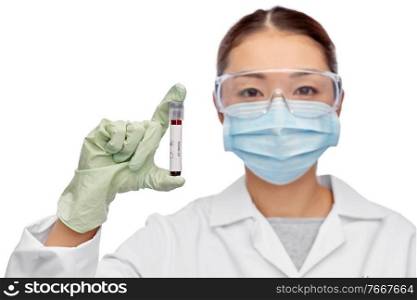 medicine, health and pandemic concept - young asian female doctor or scientist in medical mask and goggles holding beaker with blood test. asian female doctor holding beaker with blood test