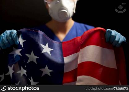 medicine, health and pandemic concept - young female doctor or nurse wearing goggles and face protective mask or respirator for protection from virus holding flag of america over black background. doctor in goggles and mask holding flag of america