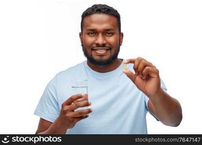 medicine, health and people concept - happy smiling african american man with pill and glass of water over white background. african american man with pill and glass of water